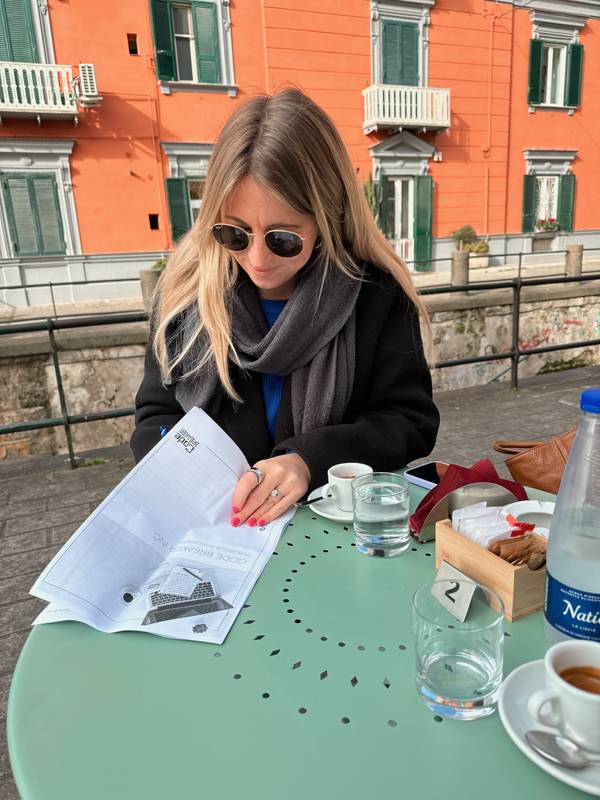Jenn reading a printed article at a café table in Rome